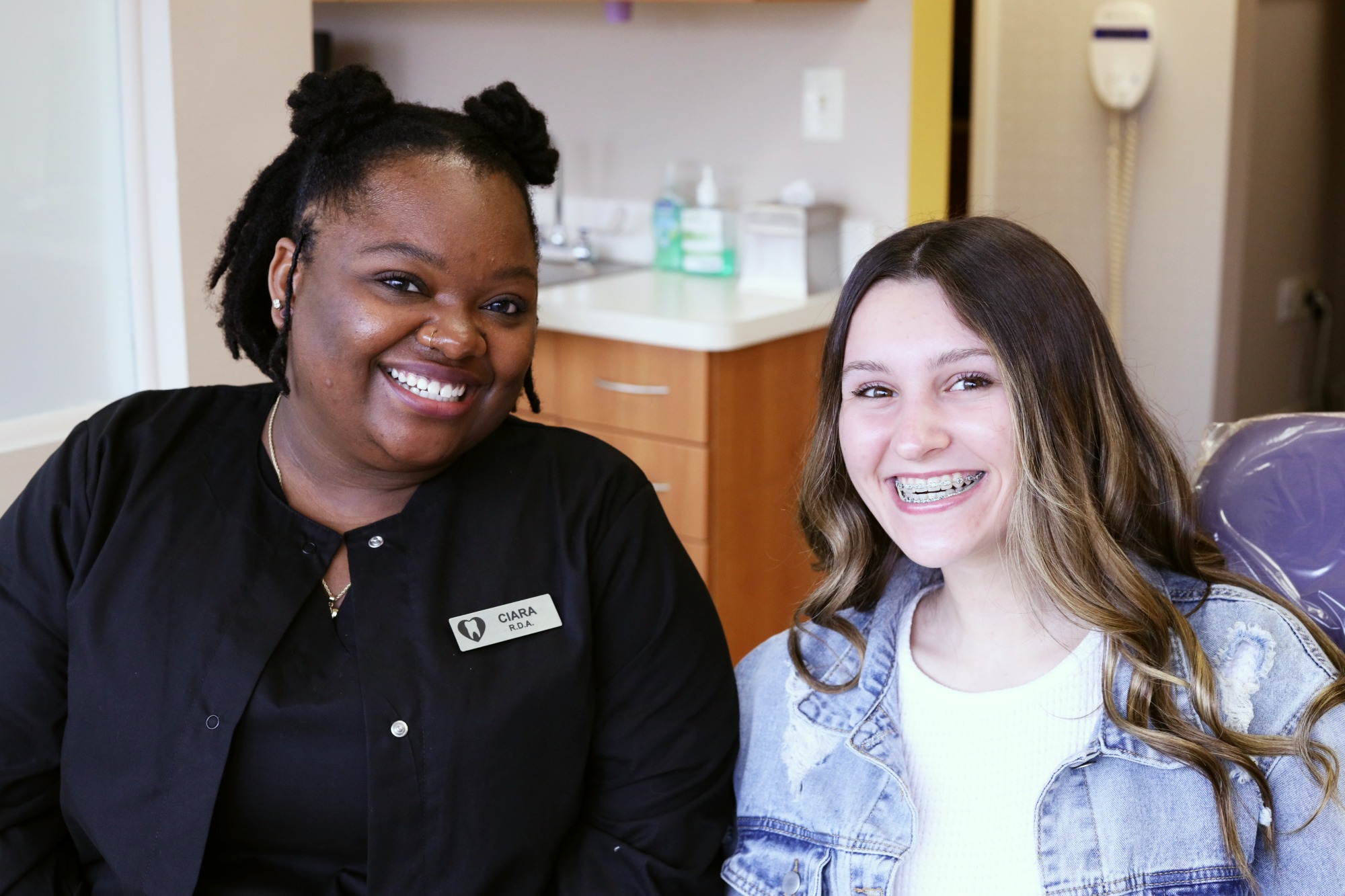 Smiling Monroe Orthodontics team member in a black uniform poses with a teen patient wearing braces at Dr. Susan Leiva’s orthodontic office in Monroe Township, NJ.