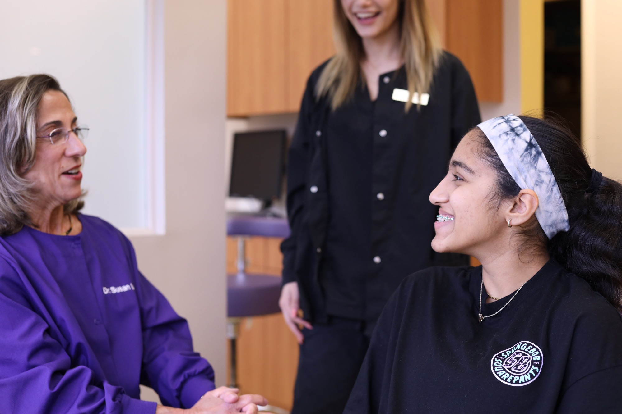 Team member in black scrubs talking with a smiling teen patient during a visit at Monroe Orthodontics, where Dr. Susan Leiva provides Monroe Township orthodontics